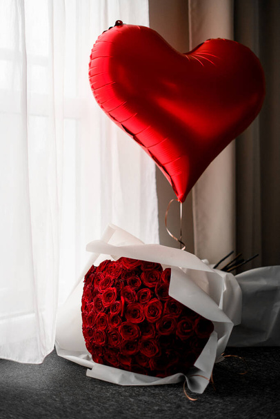 Large bouquet of red roses and heart shaped air balloon waits for loved one in room. Happy st. valentines day or date concept - Фото, зображення