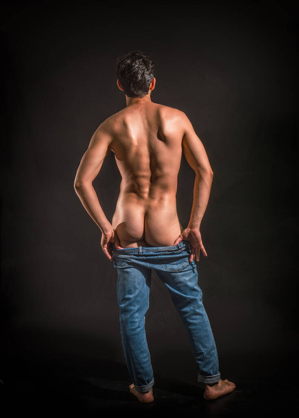 Muscular man pulling down jeans to show his butt, in studio shot - Foto, Imagem