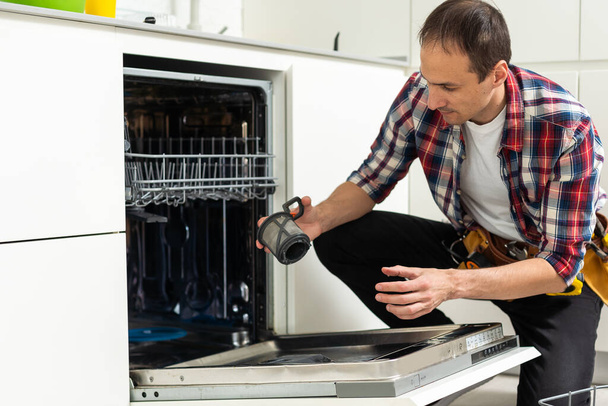 Kodinkone huolto - yleismies poistamalla likainen astianpesukone ruoka jäämiä suodatin. Laadukas kuva - Valokuva, kuva