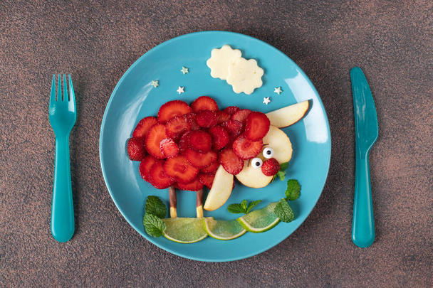 Sheep animal with strawberry, apple and lime laid out on blue plate on brown background - fun idea childrens breakfast - Zdjęcie, obraz