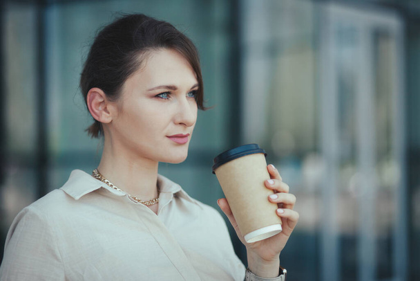Πορτρέτο της νεαρής επιχειρηματία κρατώντας σε χέρια χάρτινο κύπελλο με takeaway καφέ ή άλλο ποτό. - Φωτογραφία, εικόνα