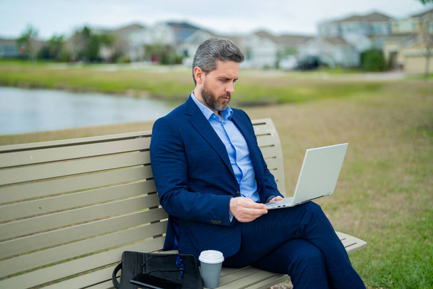 Business man in suit sitting on bench. Business man on bench in park outdoors. Thinking about business. Thoughtful businessman, freelancer work on laptop on american neighborhood. Free business - Zdjęcie, obraz