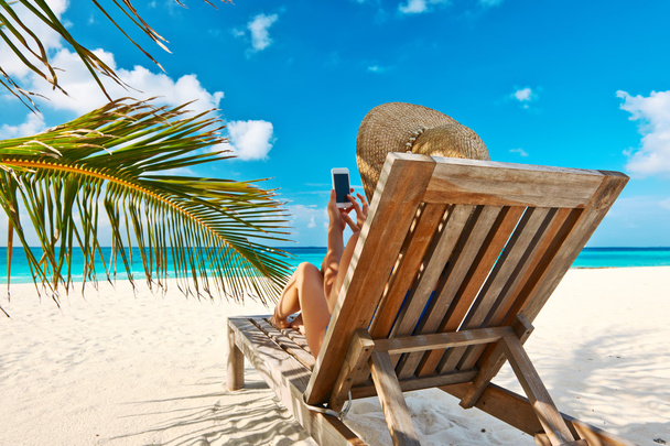 Vrouw in hoed met mobiele telefoon op strand - Foto, afbeelding