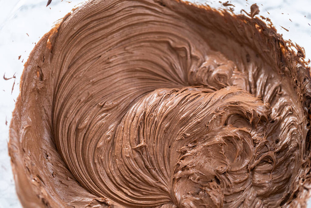 Mixing store-bought chocolate frosting in a mixing glass bowl with a hand mixer. - Fotografie, Obrázek