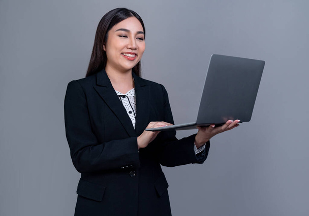 Fiduciosa giovane donna d'affari asiatica in posa con laptop su sfondo isolato. Ufficio signora fare gesto mano per le promozioni di vendita, pubblicità tecnologia o immagine di reclutamento HR. Giubilante - Foto, immagini