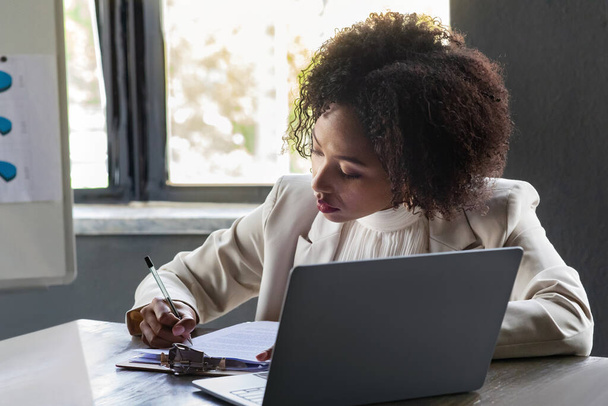 Atraktivní černošky mladá žena na sobě formální oblečení sekretářka sedí za stolem před notebookem v konferenčním sále, dělat si poznámky během pracovní schůzky v moderní kanceláři, kopírovací prostor - Fotografie, Obrázek