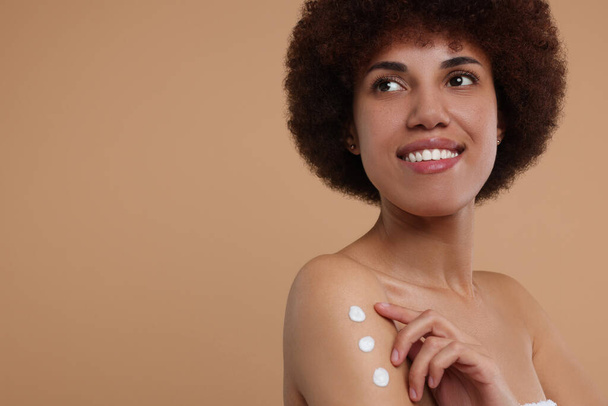 Beautiful young woman applying body cream onto arm on beige background, space for text - Photo, Image