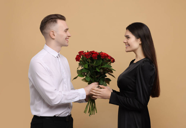Boyfriend presenting beautiful bouquet roses to his girlfriend on beige background. Valentine's day celebration - Foto, Imagem