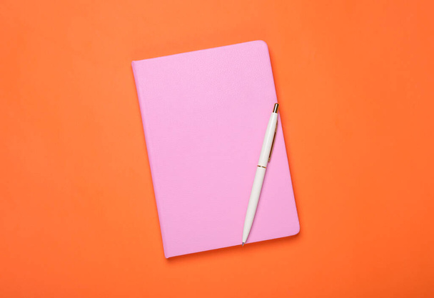 Closed pink notebook and pen on orange background, top view - Foto, immagini