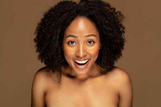 Excited emotional happy pretty half-naked millennial african american woman 30s grimacing on brown studio background, closeup. Innovative face care hacks, beauty routine concept - Foto, Imagem