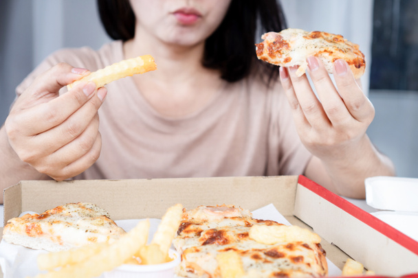 Азиатская женщина переедает пиццу и картошку фри, нездоровый образ жизни, расстройство пищевого поведения - Фото, изображение