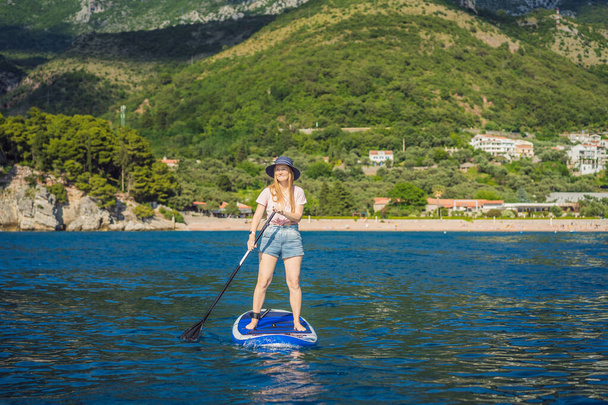 Mujeres jóvenes se divierten de pie remando en el mar de agua azul cerca de la isla de San Estefan en Montenegro. SUP. - Foto, imagen