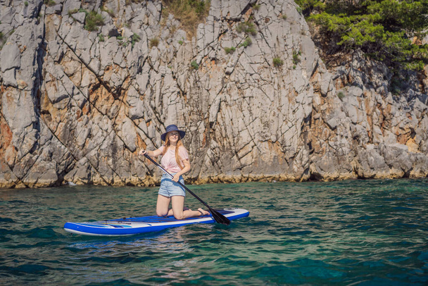 Młode kobiety Zabawa Stand Up Wiosłowanie w błękitnej wodzie wśród skał w Czarnogórze. SUP. - Zdjęcie, obraz