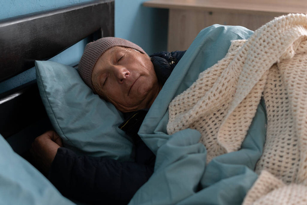 A férfi otthon fázik a fűtési problémákkal, az ágyban alszik, sok ruhát és sapkát visel. Fénymásolási hely - Fotó, kép
