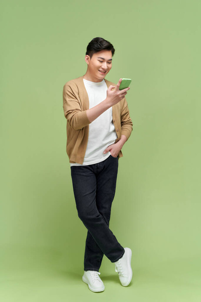 Attraktiver Mann chattet oder tippt SMS mit Handy isoliert über grünem Hintergrund - Foto, Bild