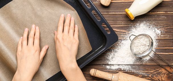 Woman putting parchment into baking tray on wooden background - Zdjęcie, obraz