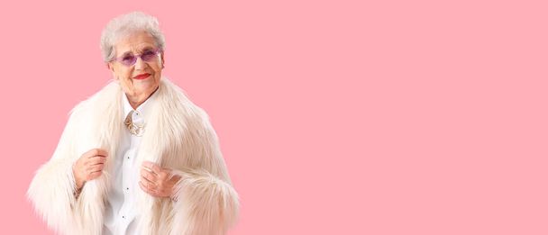 Stylish senior woman in fur coat on pink background with space for text - Photo, Image