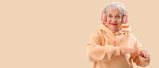 Senior woman in headphones listen to music on beige background with space for text - Valokuva, kuva