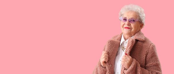 Elegante mujer mayor en peluche sobre fondo rosa con espacio para el texto - Foto, Imagen