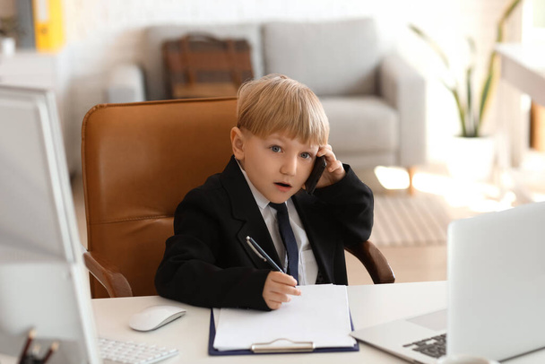 Zabawny mały biznesmen rozmawiający przez telefon komórkowy przy stole w biurze - Zdjęcie, obraz