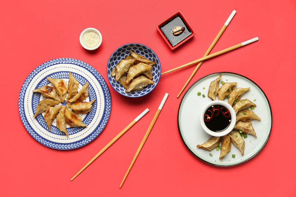Plates with tasty Chinese jiaozi and sauce on red background - Photo, image