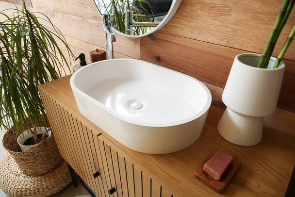 Белая раковина и ваза со стеблями бамбука на столе в ванной комнате - Фото, изображение