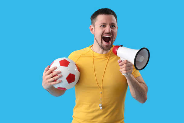Entrenador masculino con pelota de fútbol y megáfono sobre fondo azul - Foto, imagen