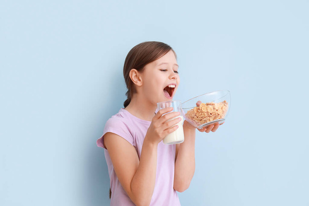 Маленька дівчинка з молоком і кукурудзяними пластівцями на світло-блакитному фоні
 - Фото, зображення