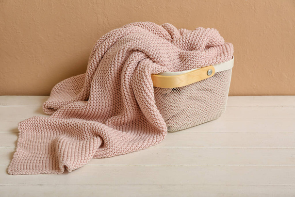 Basket with new soft blanket on table near beige wall - Foto, imagen