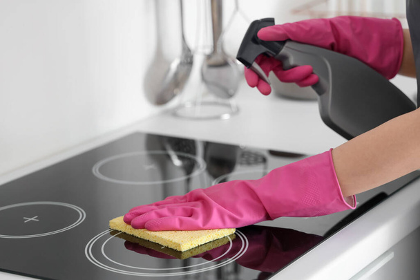 Vrouw in roze rubberen handschoenen schoonmaken elektrisch fornuis met spons en wasmiddel - Foto, afbeelding