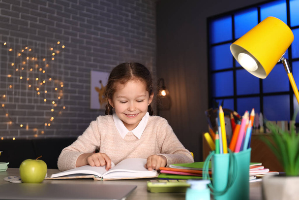 Μικρό κορίτσι διαβάζει βιβλίο στο σπίτι αργά το βράδυ - Φωτογραφία, εικόνα