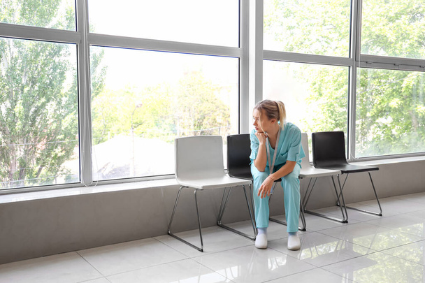 Droevige vrouwelijke medische stagiaire zit in kliniek - Foto, afbeelding