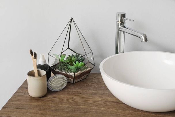 Table with sink bowl, toothbrushes and florarium in bathroom - Photo, Image