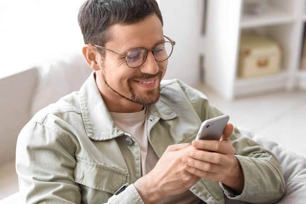 Handsome man in stylish eyeglasses using mobile phone at home, closeup - 写真・画像