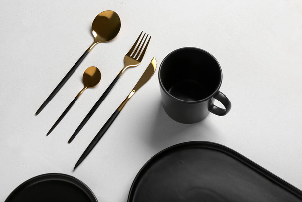 Чистые тарелки, чашки и золотые столовые приборы на сером столе - Фото, изображение