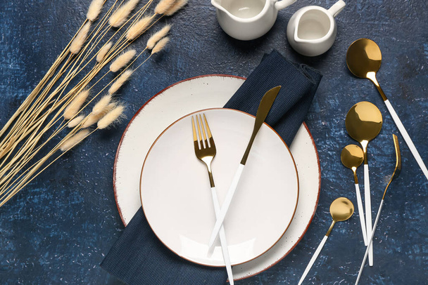 Asztalbeállítás tiszta tányérokkal, arany evőeszközökkel és szárított lagurus kék alapon - Fotó, kép