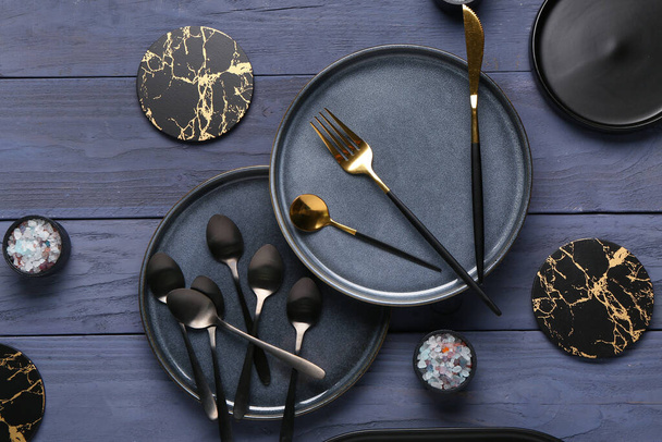 Tiszta tányérok evőeszközökkel és italalátétekkel a kék fa asztalon - Fotó, kép