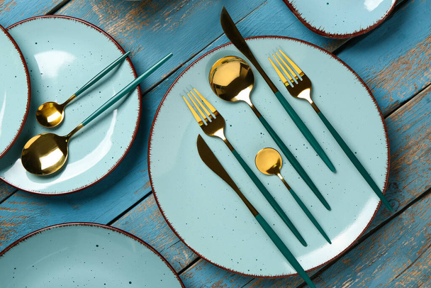 Clean plates with set of golden cutlery on blue wooden table - Фото, изображение
