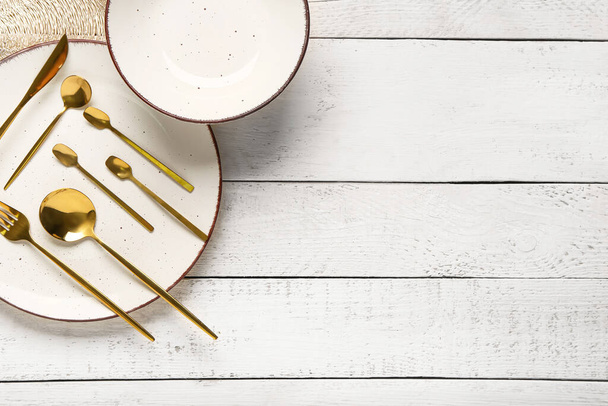Καθαρό πιάτο με σετ από χρυσά μαχαιροπίρουνα και μπολ σε λευκό ξύλινο τραπέζι - Φωτογραφία, εικόνα