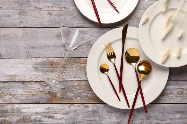 Saubere Teller mit goldenem Besteck und getrocknetem Lagurus auf verwittertem Holztisch - Foto, Bild