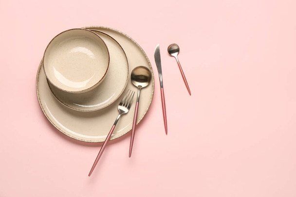 Nakrycie stołu z czystymi talerzami, miską i zestawem sztućców na różowym tle - Zdjęcie, obraz