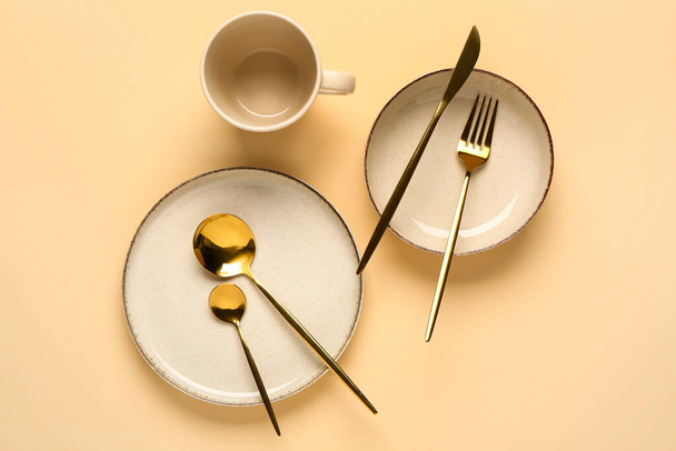 Clean plate, bowl, cup and set of golden cutlery on beige background - Photo, Image