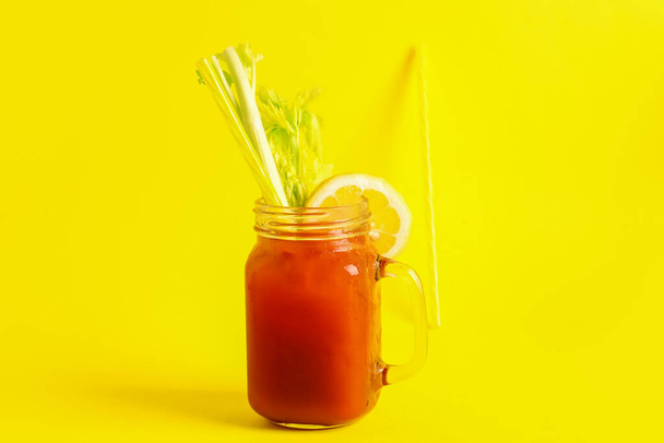 Mason jar of bloody mary with celery and lemon on yellow background - Fotó, kép