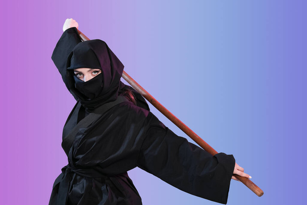 Female ninja with stick on color background - Photo, Image