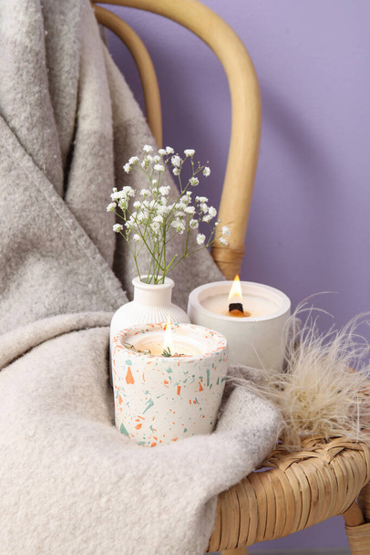 Holders with burning candles, gypsophila flowers and blanket on chair near purple wall in room, closeup - Photo, Image