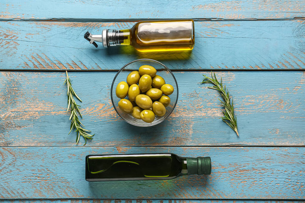 Miska z dojrzałymi oliwkami i butelkami oleju na niebieskim drewnianym tle - Zdjęcie, obraz