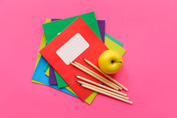 Kolorowe zeszyty ze świeżym jabłkiem i ołówkami na różowym tle - Zdjęcie, obraz