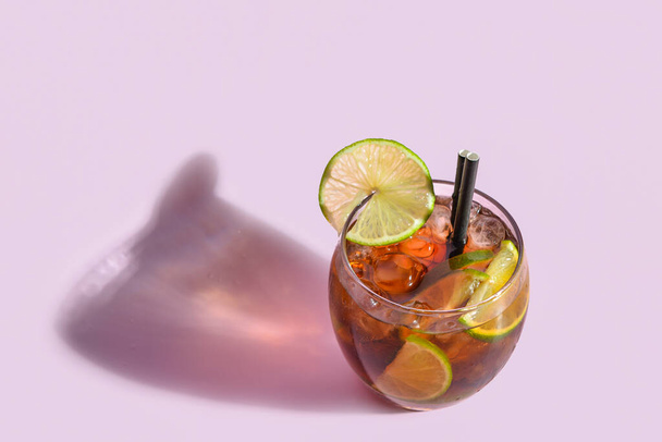 Glass of cold Cuba Libre cocktail on lilac background - 写真・画像