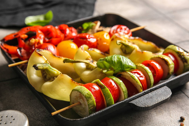 Baking dish with tasty grilled vegetables on grey tile background - Photo, Image
