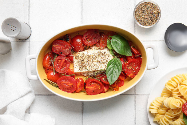 Baking dish with tasty tomatoes and feta cheese on white tile background - Photo, Image